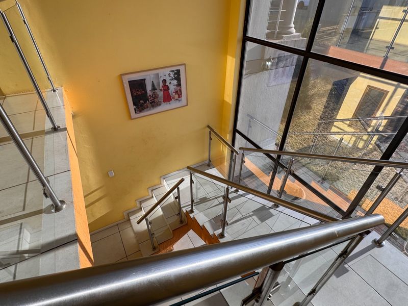A bright, open-plan staircase area featuring modern stainless steel and glass balustrades, tiled flooring, and expansive windows providing natural light.