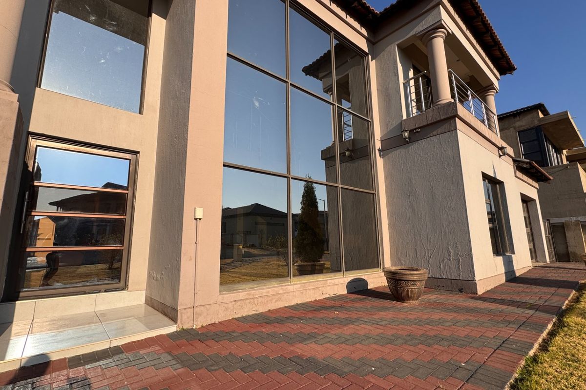 Rear elevation of a multi-story house featuring large floor-to-ceiling windows, a paved patio area, and an upper-level balcony with metal railings.