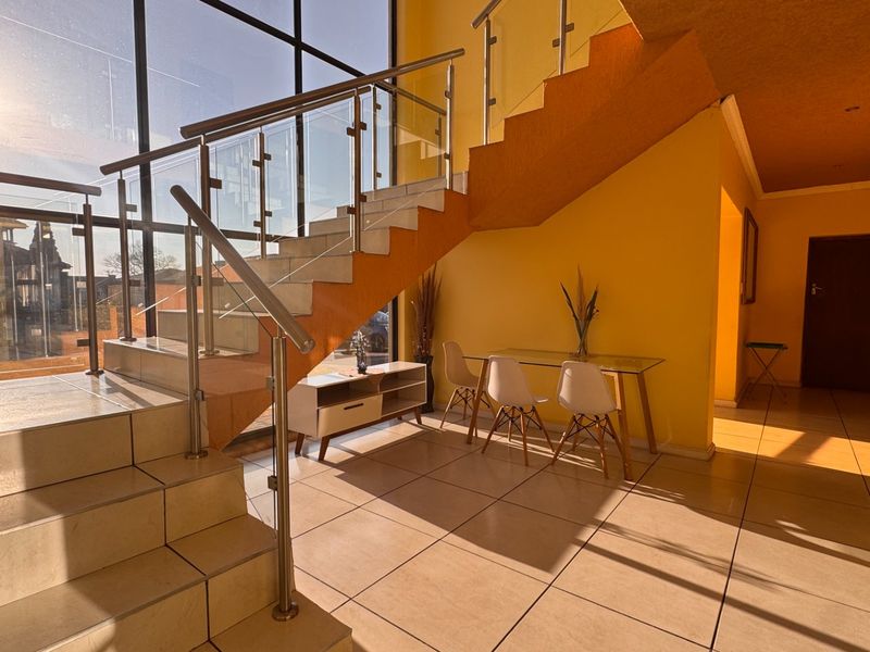 Spacious entrance hall featuring a modern staircase with glass balustrades, large windows providing ample natural light, and neutral tiled flooring.