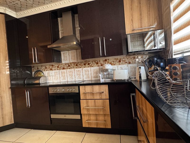 A modern kitchen featuring dark and wood-tone cabinetry, integrated appliances including an oven and extractor fan, and a mosaic tile backsplash.