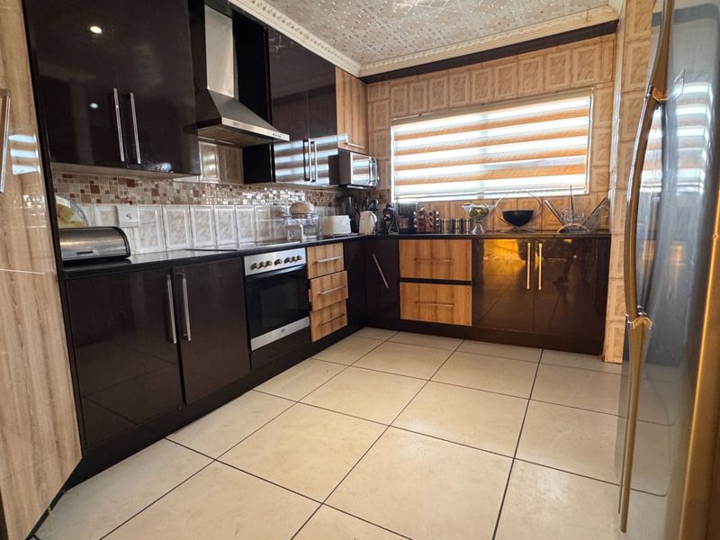 A functional kitchen featuring dark and wood-tone cabinetry, built-in oven, extractor fan, tiled backsplash, and neutral floor tiles.