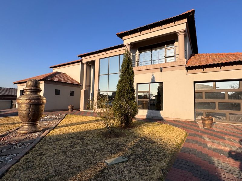 A modern double-story residential property featuring a tiled roof, large glass windows, a balcony, and a paved driveway leading to a double garage.