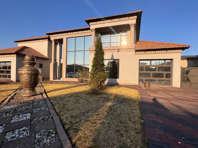A modern double-story residence featuring a large glass facade, terracotta roof tiles, a paved driveway, and an integrated double garage.