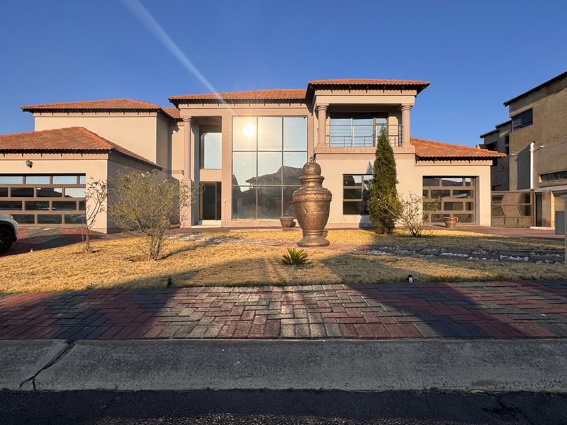 A modern double-story residential property featuring a large glass facade, tiled roof, balcony, and double garage with a paved driveway.