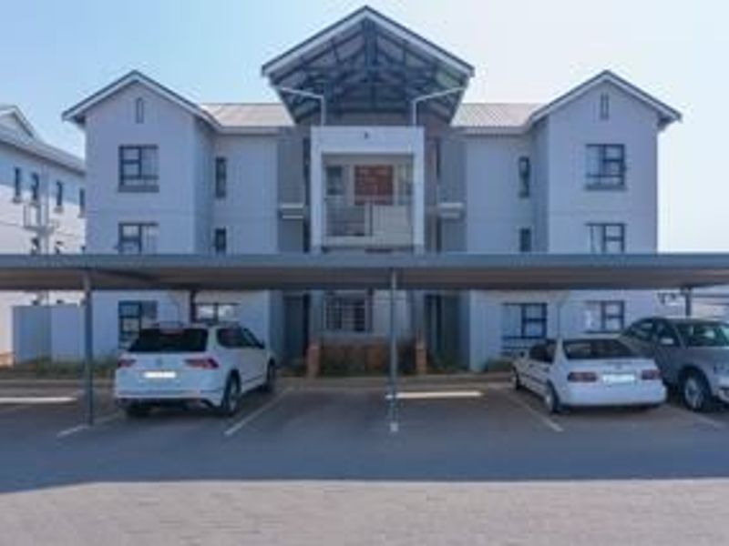 Front elevation of a modern apartment complex featuring covered parking bays and a structured facade with aluminium window frames.