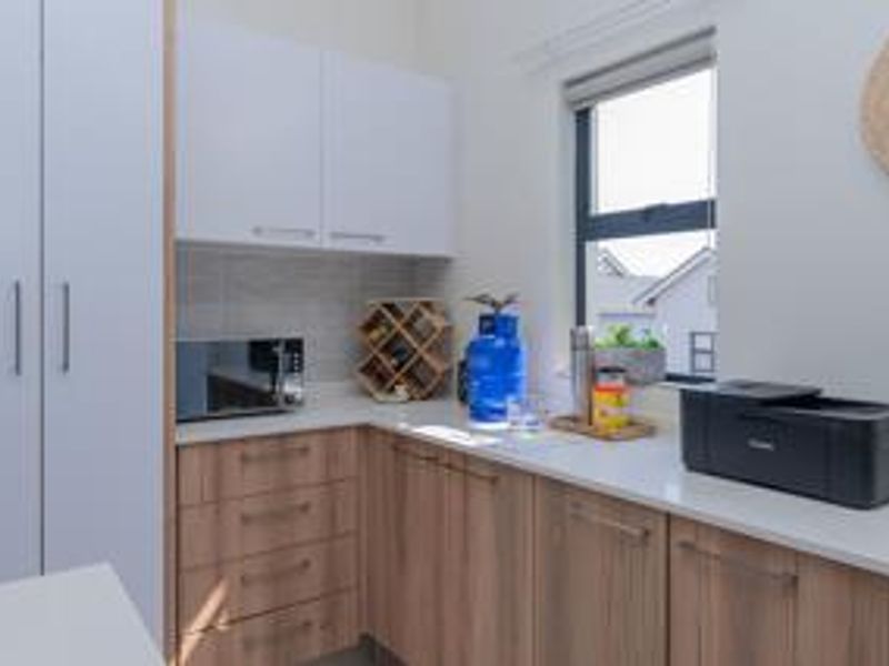 A functional scullery or utility area featuring modern wood-grain cabinetry, stone countertops, and a tiled backsplash, providing additional storage and workspace.