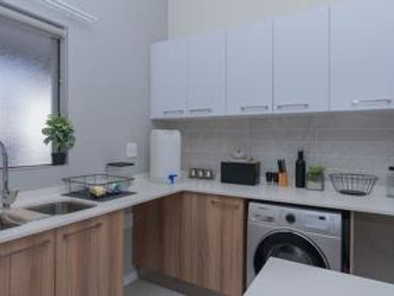 A functional laundry room featuring modern wood-finish lower cabinetry, white upper cabinets, stone countertops, and a built-in washing machine.
