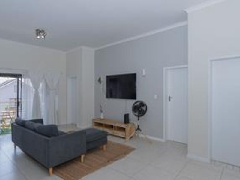 A bright living room featuring tiled flooring, neutral wall tones, and a sliding glass door providing access to an outdoor area.