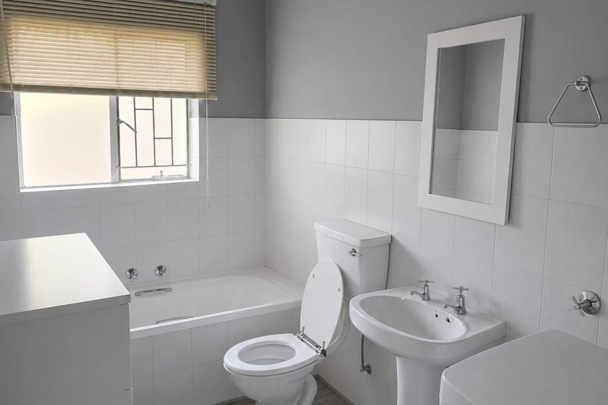 A clean, functional bathroom featuring a pedestal basin, built-in bathtub, and toilet with neutral grey and white finishes.