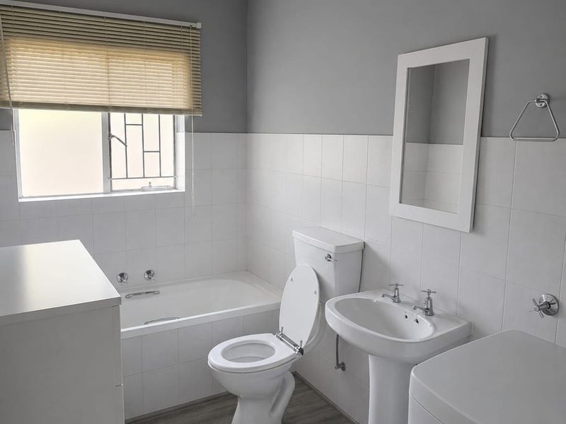 A clean, functional bathroom featuring a pedestal basin, built-in bathtub, and toilet with neutral grey and white finishes.