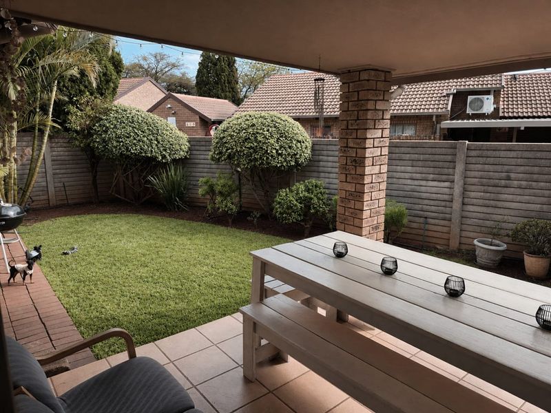 A covered patio area featuring tiled flooring and a brick support pillar, overlooking a private garden with a concrete boundary wall.