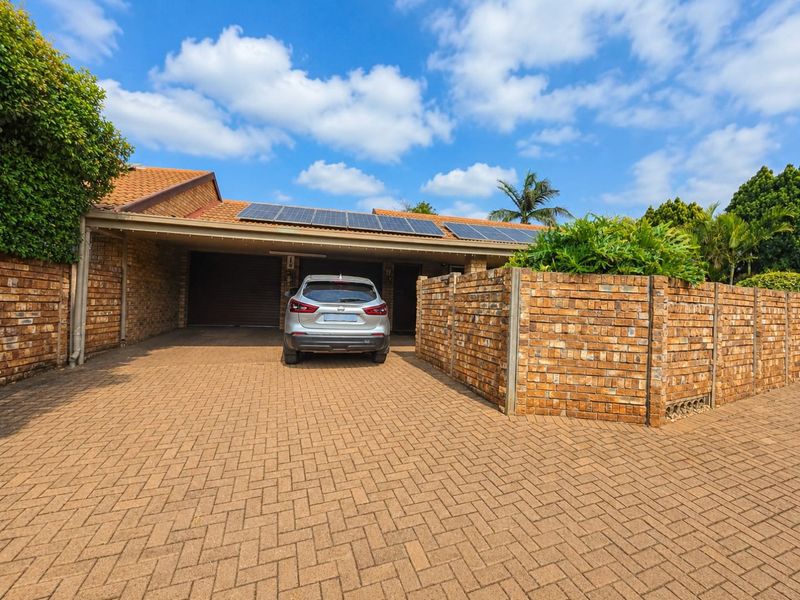 Front exterior view of a townhouse featuring a paved driveway, face brick facade, double garage, and roof-mounted solar panels.