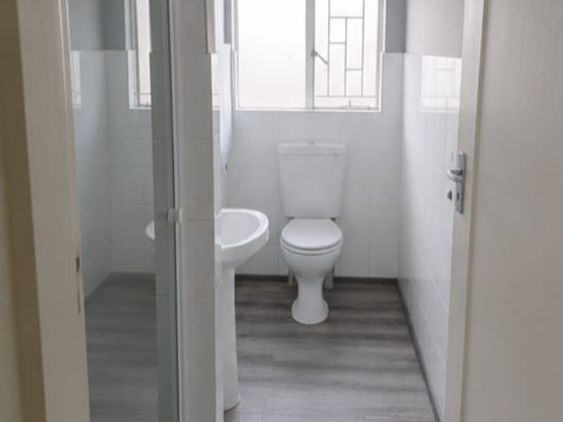 A clean, functional bathroom featuring a pedestal basin, toilet, and a glass-enclosed shower with modern laminate flooring and neutral wall finishes.