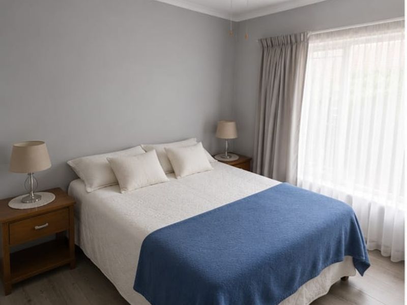 A well-maintained bedroom featuring neutral grey walls, laminate flooring, and a ceiling fan, offering a clean and comfortable living space.