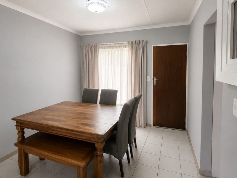 A bright and neutral dining area featuring clean tiled flooring, a flush mount ceiling light, and a solid wood door leading to an adjacent space.