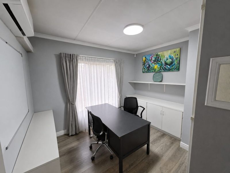 A well-maintained home office featuring built-in cabinetry, floating shelving, laminate flooring, and a split-system air conditioner.