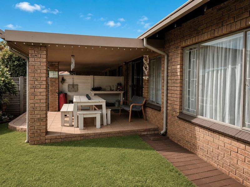 A covered brick patio area featuring tiled flooring and brick pillars, providing a functional outdoor entertainment space adjacent to the garden.