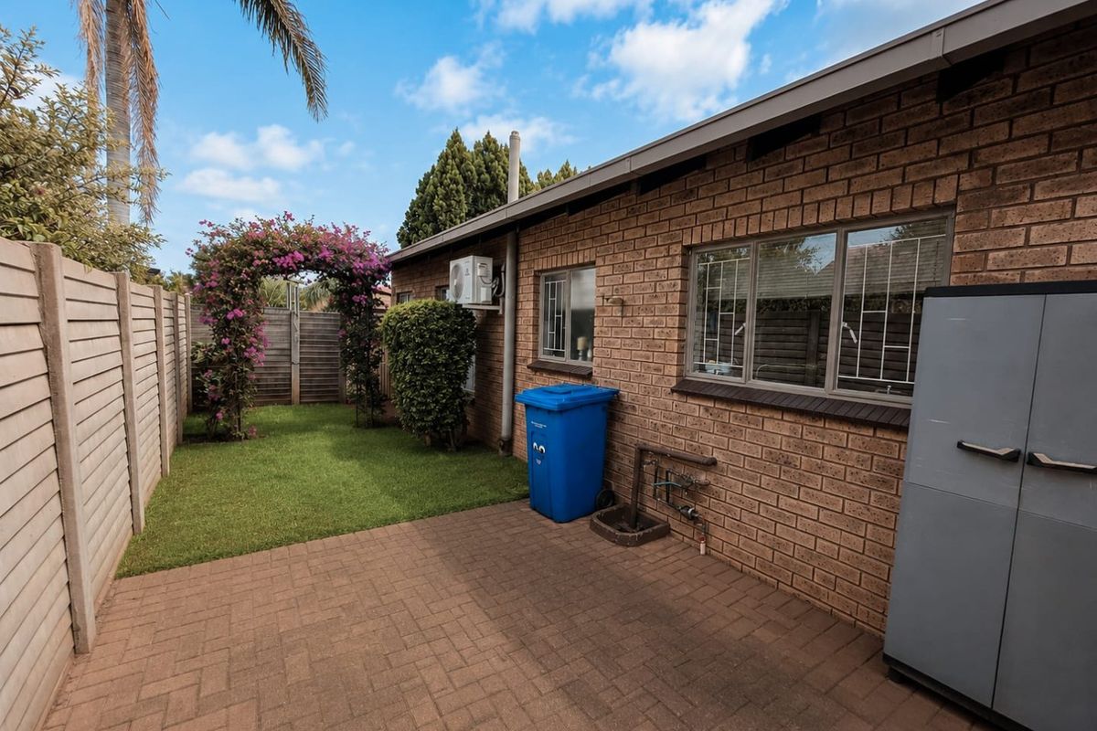 A private rear courtyard featuring a paved patio area, a small lawn, and a brick exterior facade with security-fitted windows.