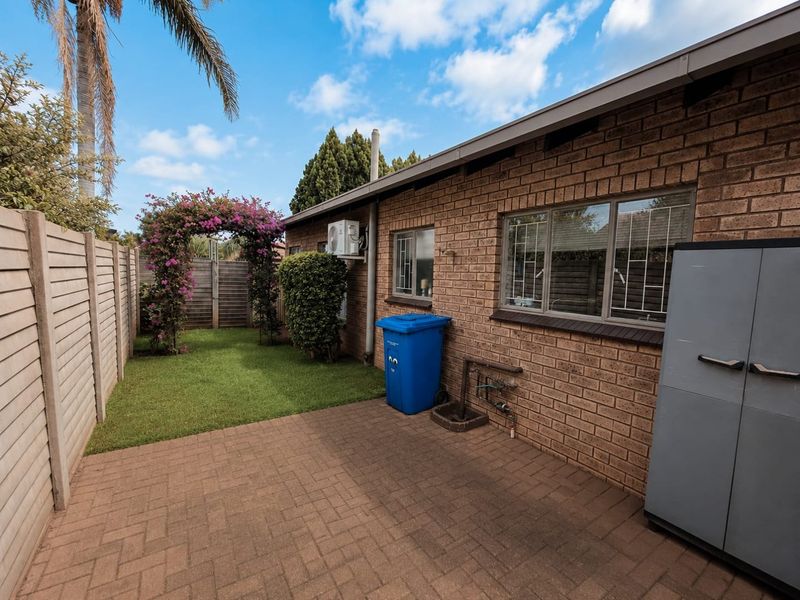 A private rear courtyard featuring a paved patio area, a small lawn, and a brick exterior facade with security-fitted windows.