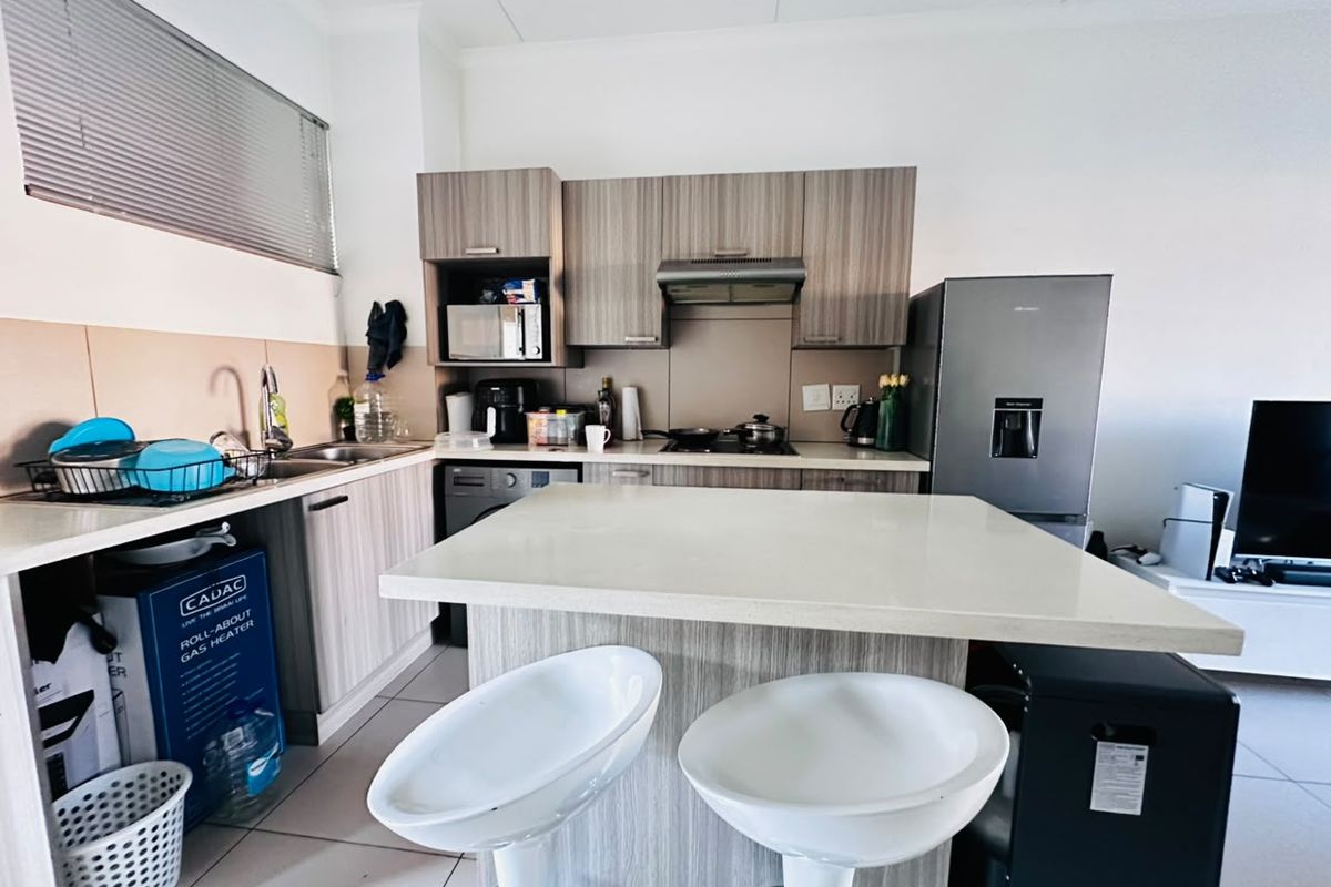 Modern kitchen featuring wood-finish cabinetry, stone countertops, integrated hob, and extractor fan, with an attached breakfast island and tiled flooring.