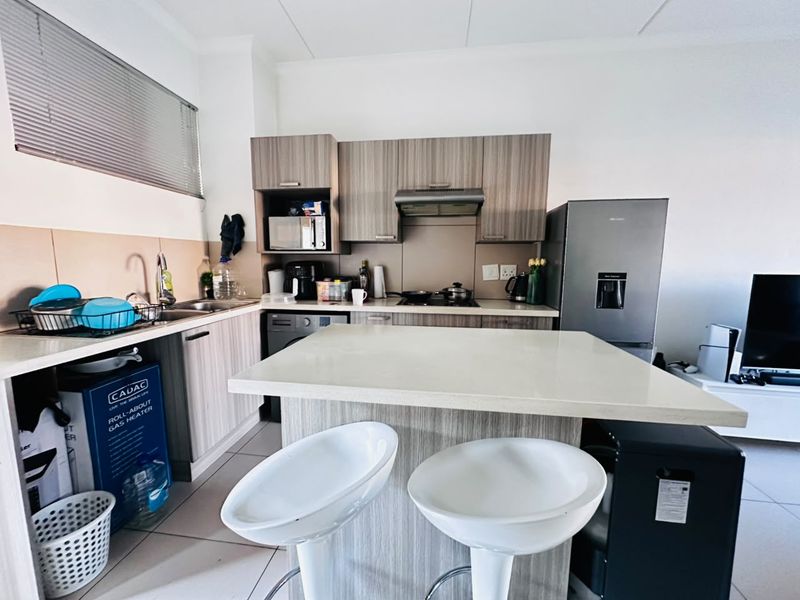 Modern kitchen featuring wood-finish cabinetry, stone countertops, integrated hob, and extractor fan, with an attached breakfast island and tiled flooring.