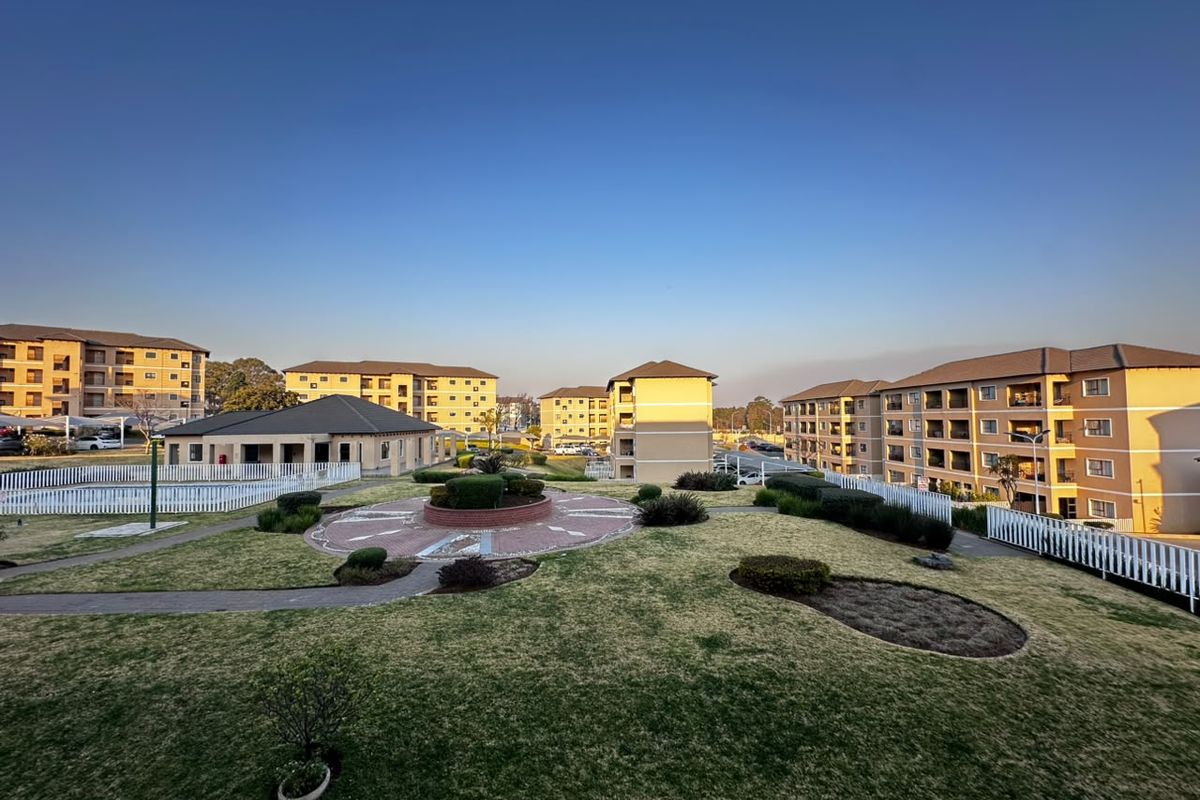 A wide-angle view of a well-maintained apartment complex featuring landscaped communal gardens, paved walkways, and multiple residential buildings.