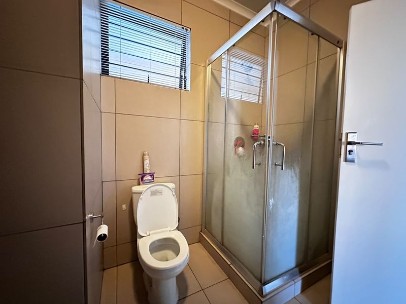 A functional bathroom featuring a glass shower enclosure, toilet, and neutral wall and floor tiling.