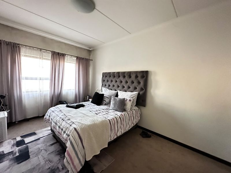 A standard bedroom featuring neutral walls, carpeted flooring, and large windows with curtain rails, providing a functional and well-lit living space.