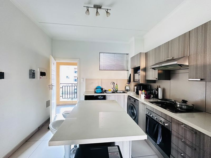 Modern kitchen featuring wood-finish cabinetry, stone countertops, a central island, and integrated appliances, with direct access to an outdoor balcony area.