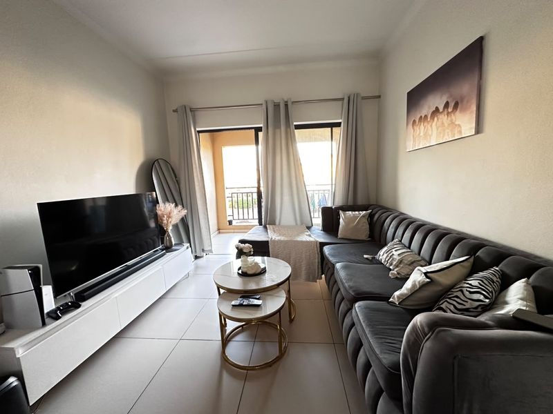 A well-maintained living room featuring large format floor tiles and a sliding glass door providing direct access to an outdoor balcony area.