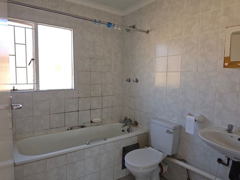 A dated bathroom featuring a standard bathtub, toilet, and pedestal basin with tiled walls, requiring cosmetic updates and grout restoration.