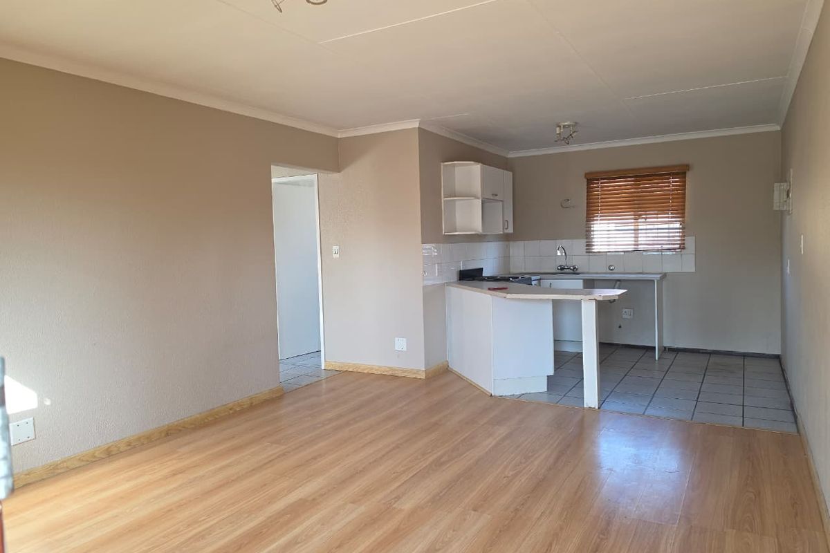 Open-plan living area featuring laminate flooring and an adjoining kitchen with built-in cabinetry, tiled splashback, and a functional sink area.