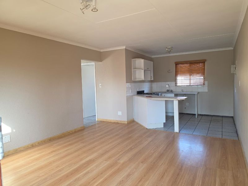 Open-plan living area featuring laminate flooring and an adjoining kitchen with built-in cabinetry, tiled splashback, and a functional sink area.
