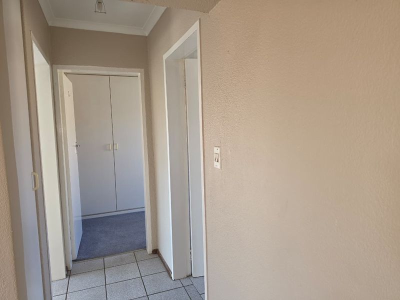 A functional hallway featuring tiled flooring, leading to a bedroom with built-in cupboards and carpeted flooring.