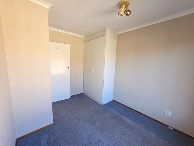 An empty bedroom featuring neutral walls, carpet flooring, and a built-in wardrobe, offering a blank canvas for personalization.
