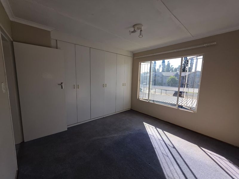 A vacant bedroom featuring built-in cupboards, carpeted flooring, and large windows with security bars, offering a blank canvas for personalization.