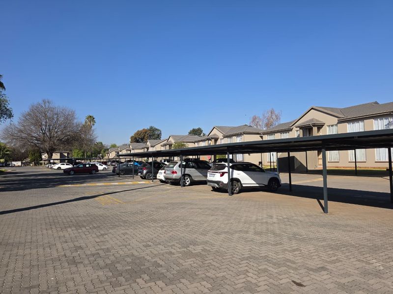 Exterior view of the apartment complex featuring a paved parking area with covered carports and well-maintained building facades.