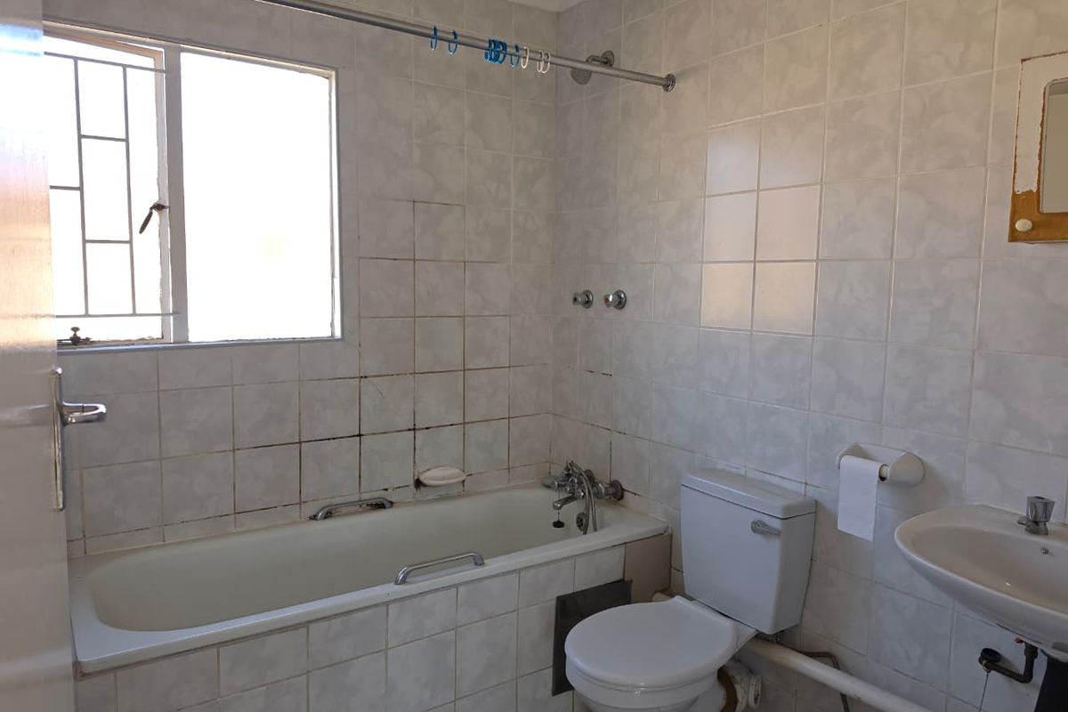 A dated bathroom featuring a bathtub, toilet, and pedestal basin with fully tiled walls and security bars on the window.