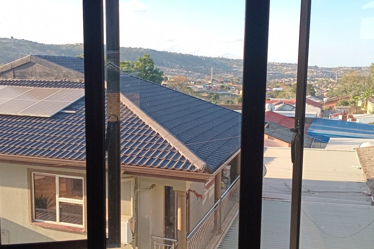 An elevated view from a window overlooking neighbouring residential rooftops and the surrounding landscape.