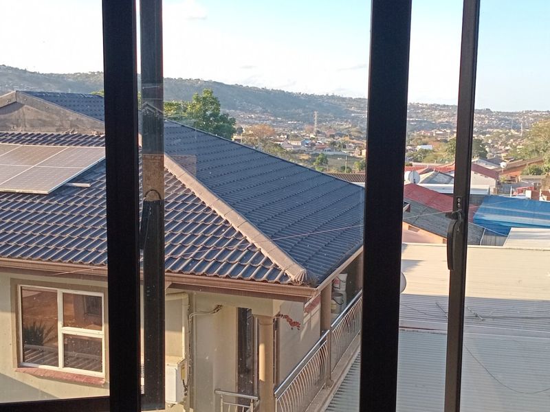 An elevated view from a window overlooking neighbouring residential rooftops and the surrounding landscape.