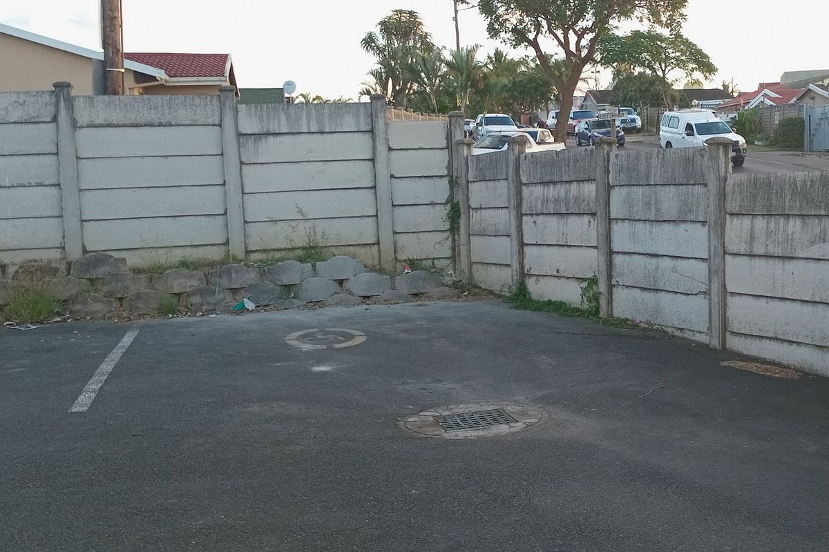An outdoor paved area featuring a precast concrete boundary wall, a retaining wall, and a stormwater drain, showing signs of weathering and wear.