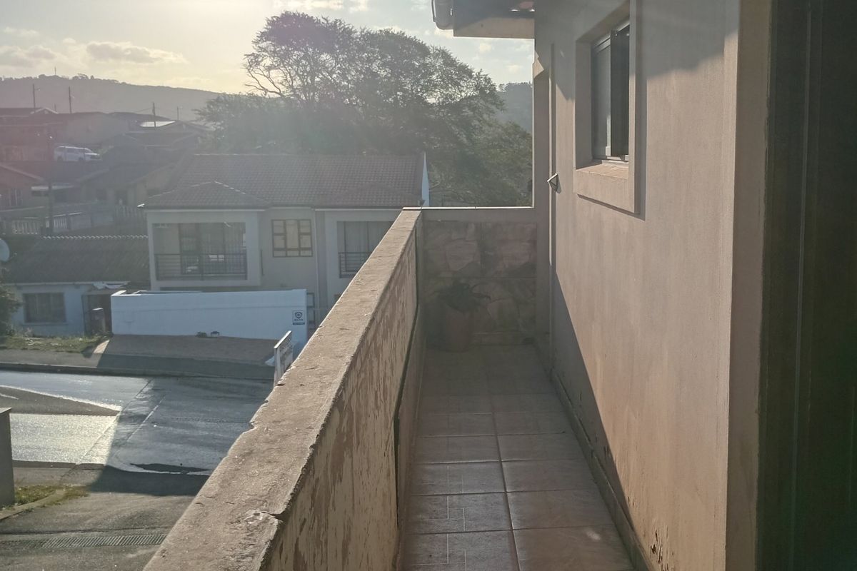 An outdoor balcony featuring tiled flooring and a masonry balustrade with stone cladding, offering an elevated view of the surrounding neighborhood.