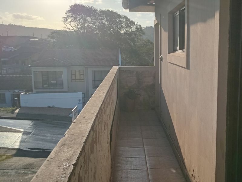 An outdoor balcony featuring tiled flooring and a masonry balustrade with stone cladding, offering an elevated view of the surrounding neighborhood.