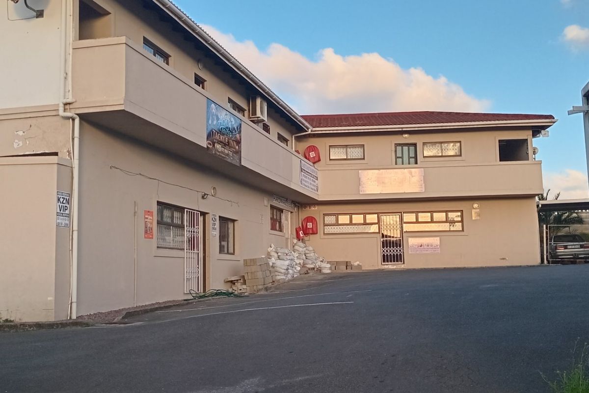 Front exterior view of a multi-level apartment building featuring an asphalt driveway, security fencing, and visible signage for commercial tenants.