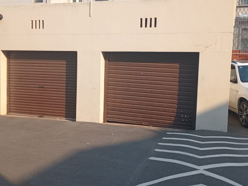A row of three secure roller shutter garage doors with an asphalt driveway and perimeter security fencing.