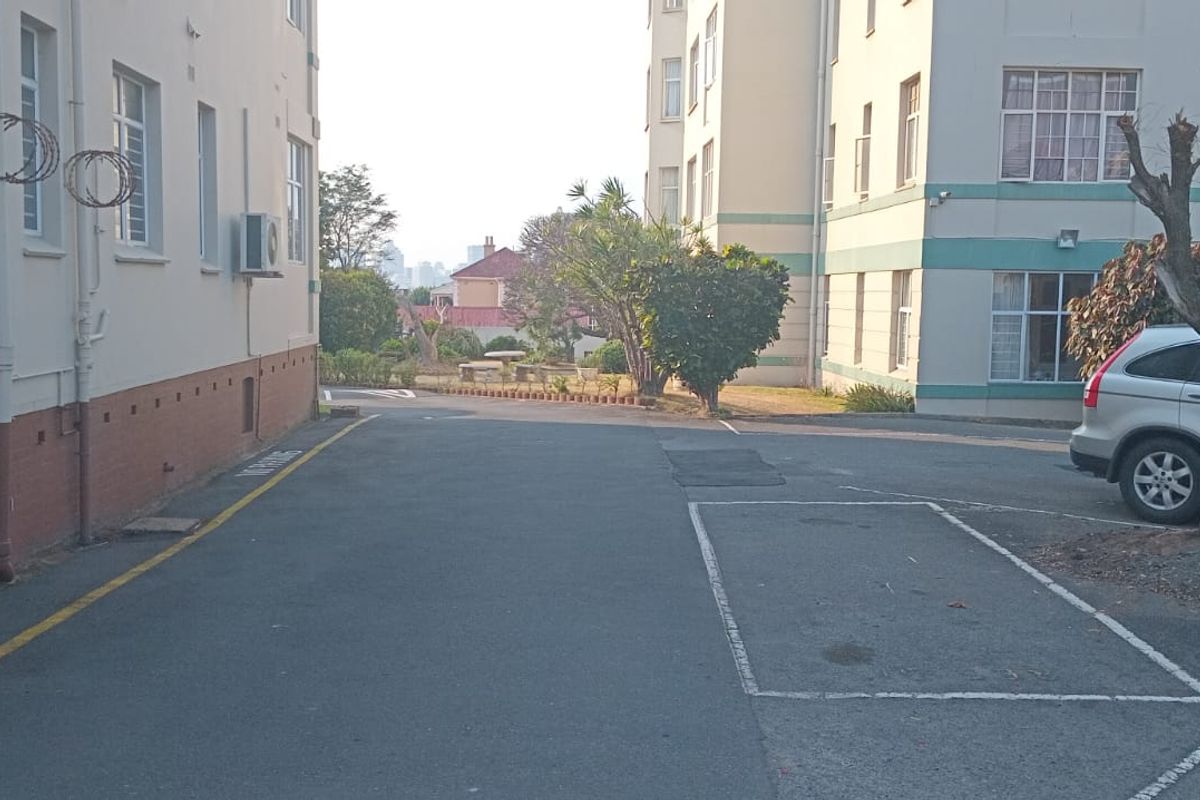 Exterior view of the apartment complex showing the rear driveway, marked parking bays, and building facade with external air conditioning units.