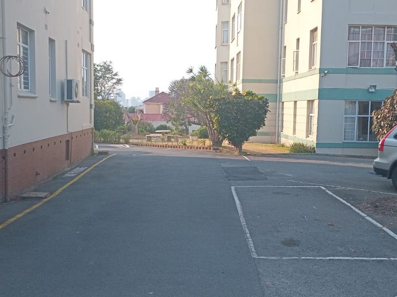 Exterior view of the apartment complex showing the rear driveway, marked parking bays, and building facade with external air conditioning units.