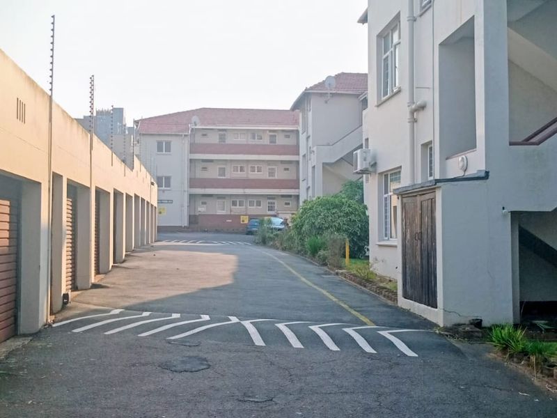Exterior view of the apartment complex featuring a row of garages, paved driveway, and external stairwell access.