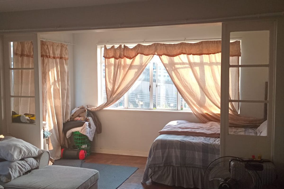 A bedroom featuring parquet flooring and a large window, partitioned by a built-in room divider, offering a functional layout with natural light.