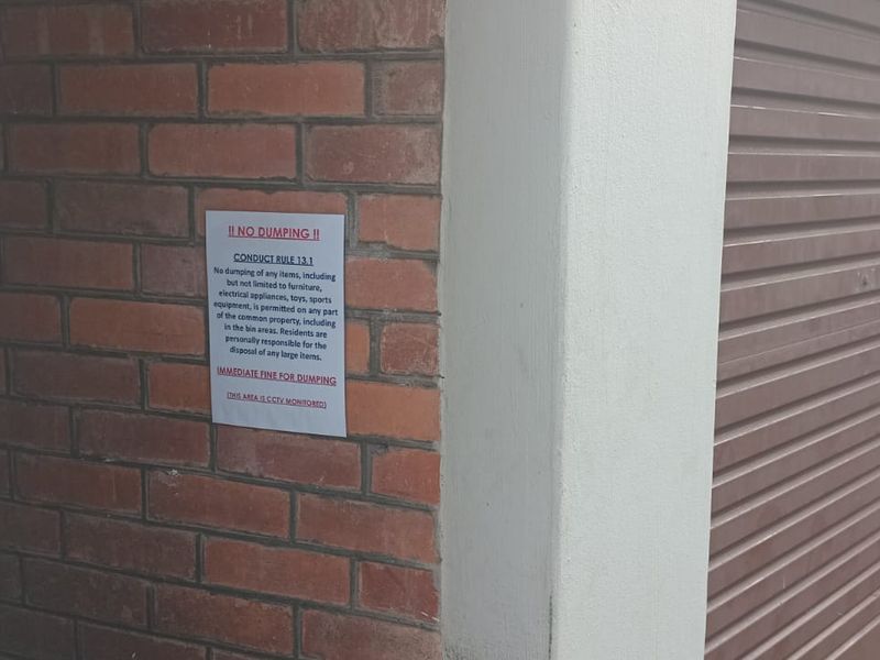A view of a garage entrance featuring a brick wall and a roller shutter door with a posted conduct notice.